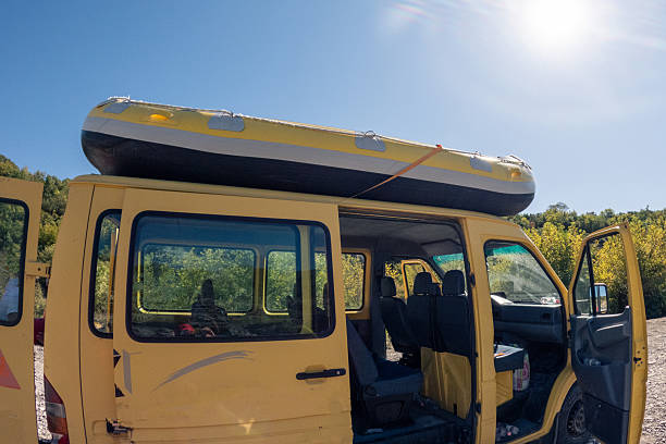 Yellow van parked outdoors with open doors and inflatable boat strapped on roof. Vehicle ready for outdoor adventure or water activities. Transport and travel concept with nature background.