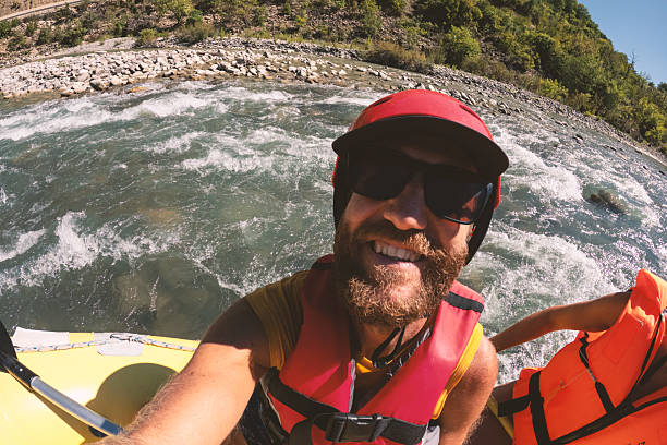 Man and woman wearing helmets and life jackets smiling on a raft in a fast-flowing river. Happy couple enjoying outdoor white water rafting activity. Adventure sports and nature recreation.