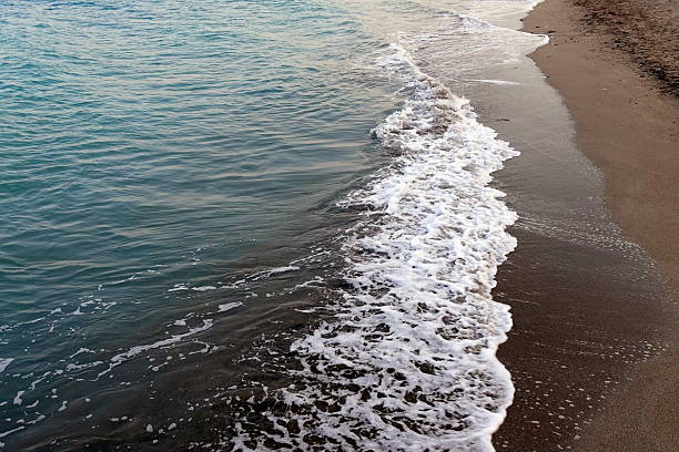 The waves rolling onto the sandy shore at sunset is a picture full of beauty and tranquility. The wet sandy beach at sunset becomes a mirror in which all the colors of the setting sun are reflected. This creates a surreal effect where the sky seems endless. The white foam on the crests of the waves contrasts brightly with the warm colors of the sunset, creating the effect of sparkling gold.