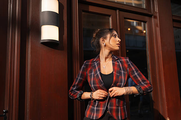 Young woman buttoning a plaid blazer on a city street, chic professional style and confident urban sophistication in natural light