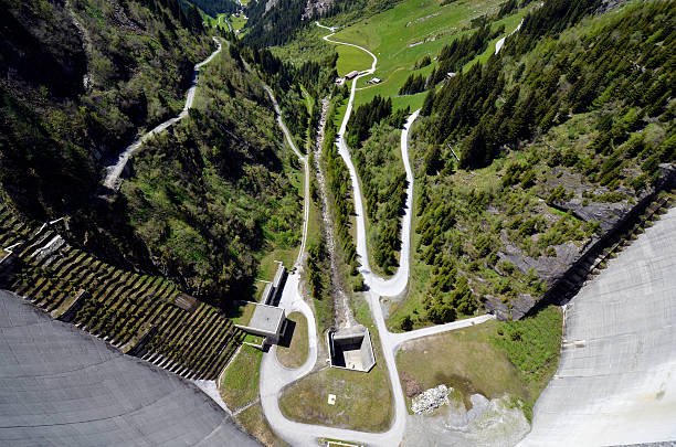 Drone view of the dam wall at Totensee lake, located on the Grimsel Pass in the Swiss Alps. The image captures the contrast between the turquoise reservoir and the rugged alpine terrain, showcasing natural beauty and hydroengineering in a high-altitude mountain setting.