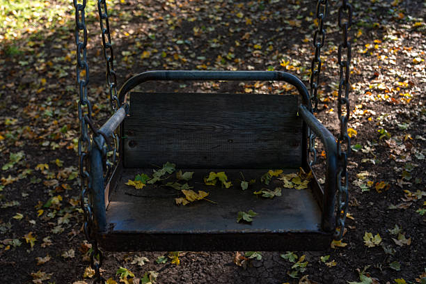 Rusty old swing in autumn forest with fallen leaves on the ground