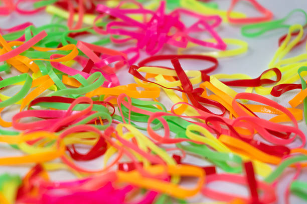 A close-up, macro shot of many vibrant and colorful rubber bands scattered on a white background, creating a playful and chaotic abstract texture.