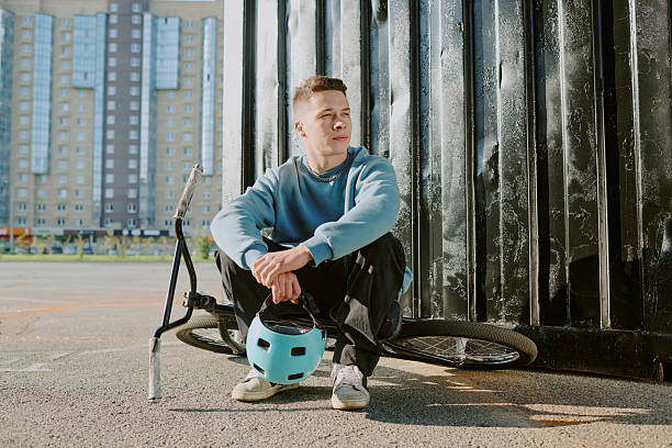 istock Teenage Boy Sitting Outdoors Holding Bicycle Helmet Resting 2242350570
