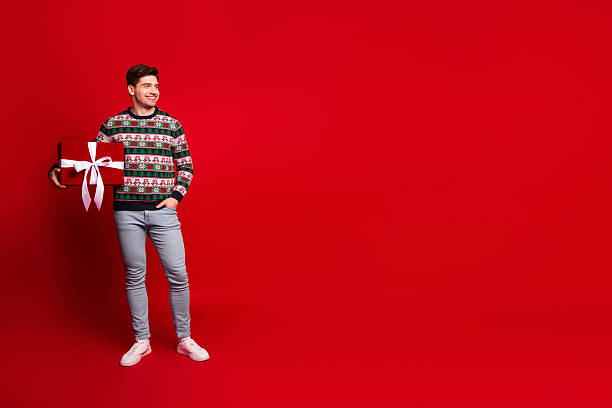 istock Cheerful man with gift posing in a bright red studio celebrates Christmas with a festive sweater and big smile for holiday shoppers and warm seasonal vibes 2242352437