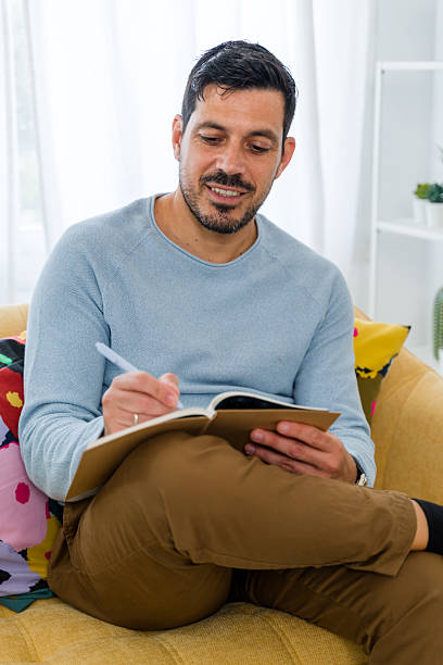istock Man writing in notebook on couch at home, smiling 2242354509