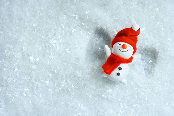 Flat lay of a snowman on artificial snow making a snow angel. Clean winter christmas background with copy space for posters, social media and winter fun concepts.