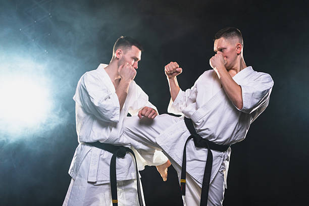 istock Martial arts masters on dark background. Strong man fighters in white kimono for karate martial arts fighting training in black gym, Karate fighters training punches kicks practicing fight sparring 2242361352