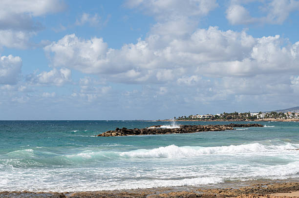 A beautiful and tranquil beach view showcasing gentle waves lapping on a rocky coastline beneath a soft, cloudy sky