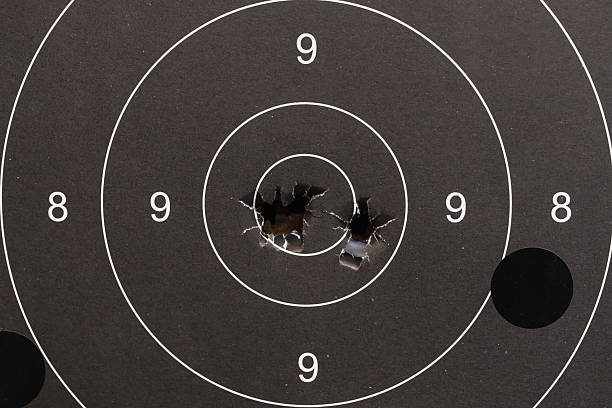 istock Used black paper shooting target showing excellent accuracy with multiple shots clustered in the center 9-ring and bullseye. 2242365044