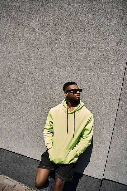 istock Young man sporting stylish attire leans against a wall on a sunny day 2242366594