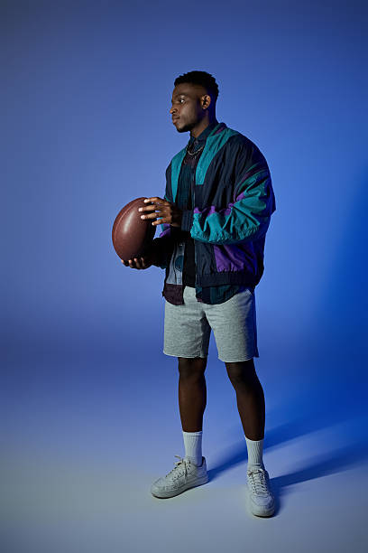 istock Stylish young man posing confidently with a football against a blue backdrop 2242367206