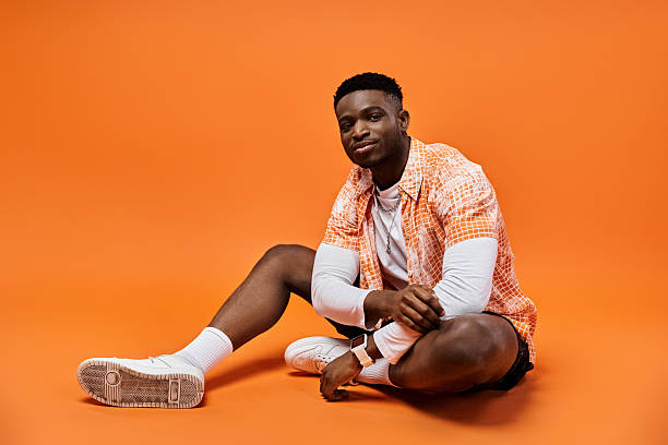 istock Young man showcases trendy style against vibrant orange backdrop in relaxed pose 2242367272