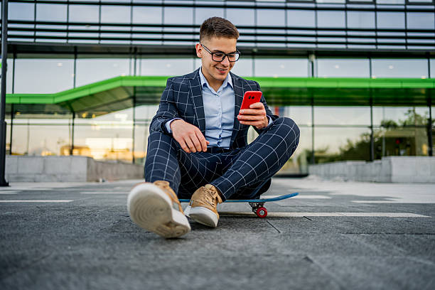 istock Young businessman sitting on skateboard checking smartphone 2242367873