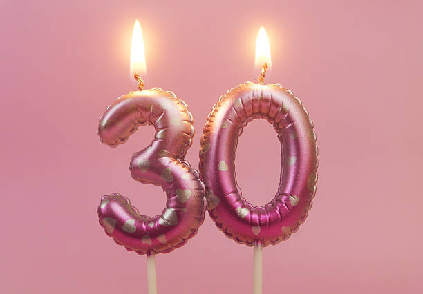 Burning air balloon shaped birthday candles with hearts on pink background, number 30