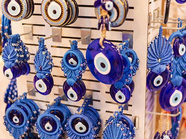 istock Rows of blue glass evil eye ornaments hang on a display rack. Each ornament features unique designs and reflects light, creating an eye-catching visual. The shop setting is bright and inviting 2242368195