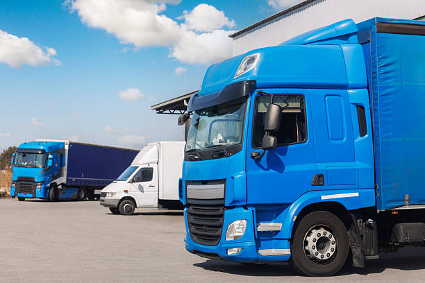 istock Modern blue cargo truck delivery van parked logistics warehouse center complex building exterior bay. Semi-trailer lorry unload goods distribution blue sky. Cargo storage facility industry building 2242368922
