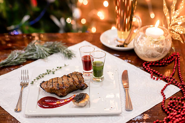 Grilled meat steak with colorful sauces and hot drink on festive table with Christmas lights.
