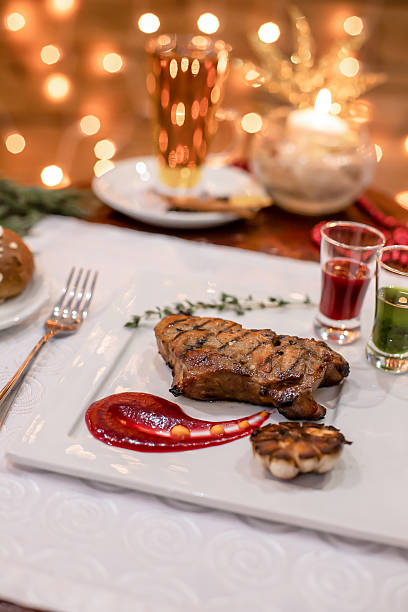 Grilled meat steak with red sauce, herbs, and roasted garlic on elegant white plate festive dinner setting.