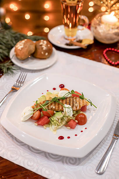 istock Grilled fish salad with mozzarella, cherry tomatoes, and pine nuts on elegant white plate festive setup. 2242370127