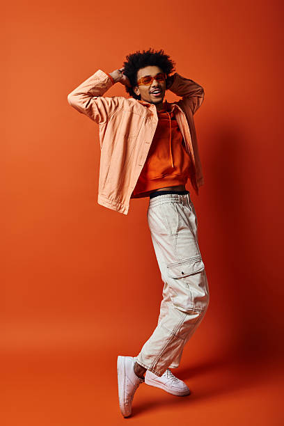 istock Young man in a trendy outfit strikes a playful pose with a bright orange backdrop, showing emotion 2242381467