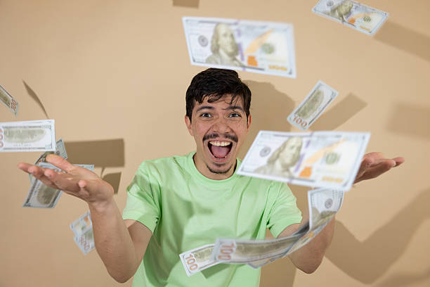 istock Smiling young man with falling bills against a light brown background 2242381670