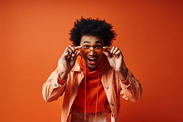 istock Young stylish man expresses joy while posing against a vibrant orange background 2242382150