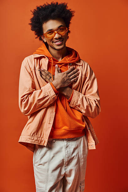istock Stylish young man expressing joy against a vibrant orange backdrop 2242382381