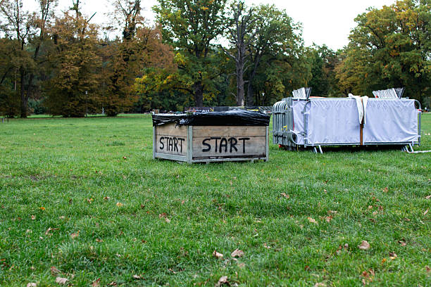 Two wooden boxes marked with the word start are set on green grass in a park. Surrounding trees showcase vibrant autumn colors, indicating a seasonal outdoor event.