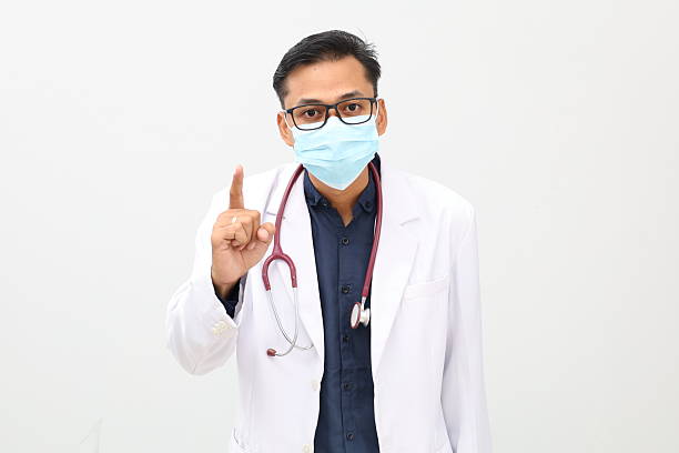 istock Young asian doctor standing wearing face mask while giving a warning. Isolated on white background 2242391096