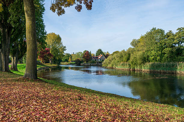 Autumn view across calm water towards Villa Augustus in Dordrecht, surrounded by open space, colourful trees, and natural beauty under soft seasonal light.