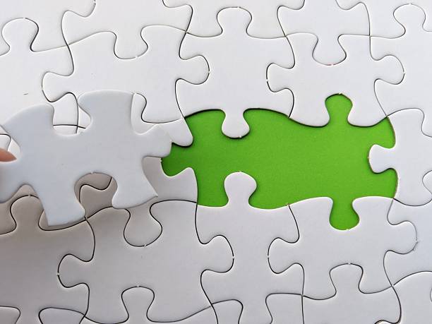 A hand places a white puzzle piece into a white puzzle with a green gap, illustrating problem solving, teamwork and finding the missing piece in a project or collaboration