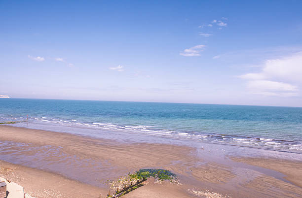 Landscape view over coastal beach english seaside scenery looking out to sea with clear blue sky background and distant horizon