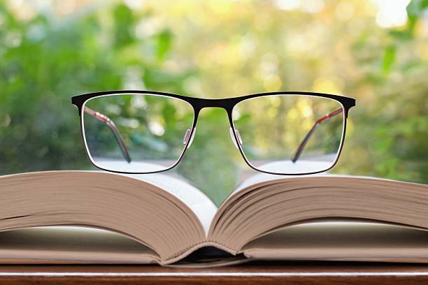 istock Reading glasses lying on the open book, natural greenery on the background 2242399302