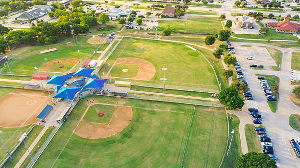 istock Batting cage in baseball park with covered bleachers, active players. Cloverleaf field layout supports multiple games. Busy parking lot reflect high community engagement, Highland Village, Texas 2242400569