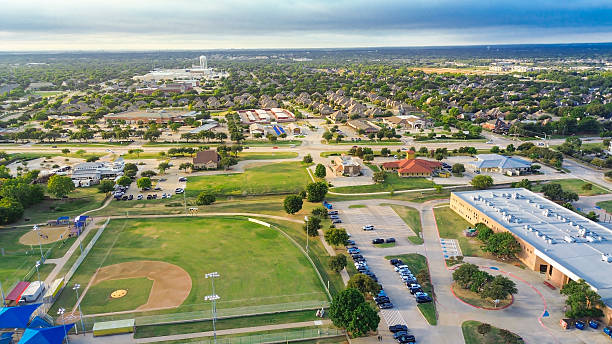 istock School campus with adjacent baseball field, soccer pitch, playgrounds. Blue and red-roofed pavilions, wide roads, church, residential homes form cohesive suburban landscape in Highland Village 2242400577
