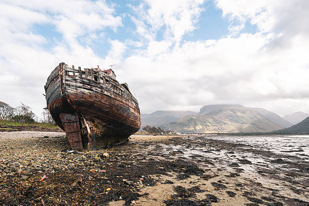 Abandoned boat decaying on a scottish beach with mountains in the background