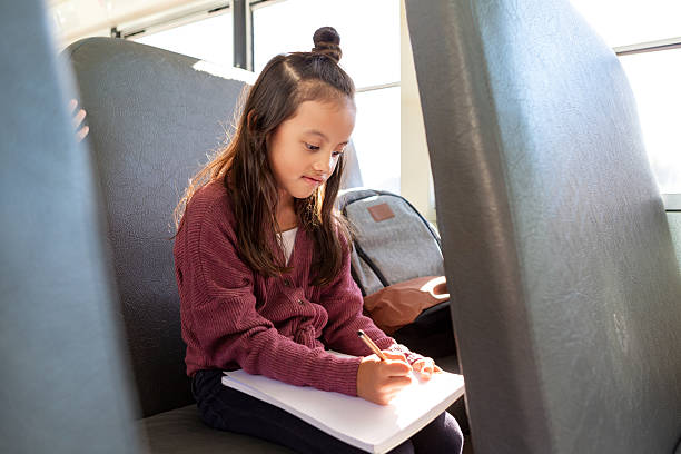 istock Young student focused on writing in a notebook while sitting on a school bus. 2242402445