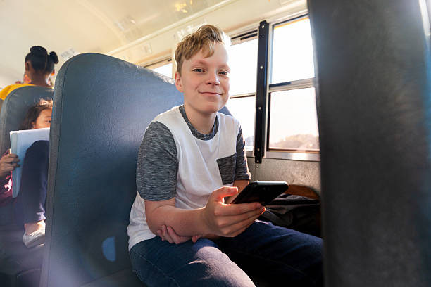 istock Young boy using a smartphone while riding on a school bus with other students present. 2242402498