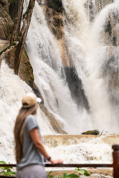 istock Woman admiring powerful natural Kuang si waterfall cascading down rocks 2242405112