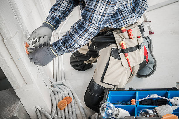 An electrician is crouched down, fixing an electrical outlet in a home. Tools are organized nearby, showcasing a focus on safety and precision.