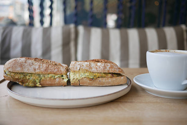 Two halves of a sandwich filled with eggs sit beside a cup of coffee.
