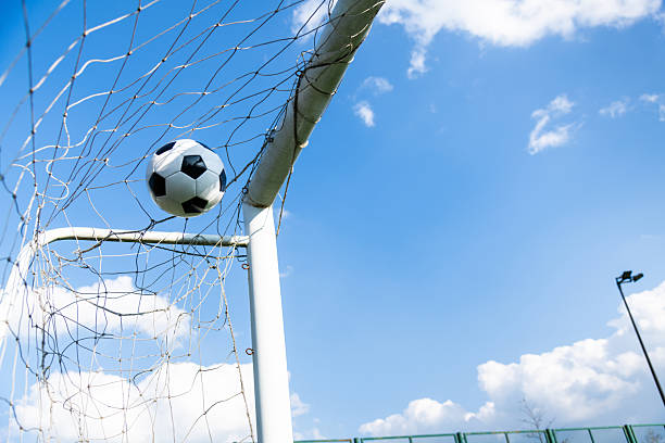 istock Soccer ball hitting the net against blue sky 2242410172