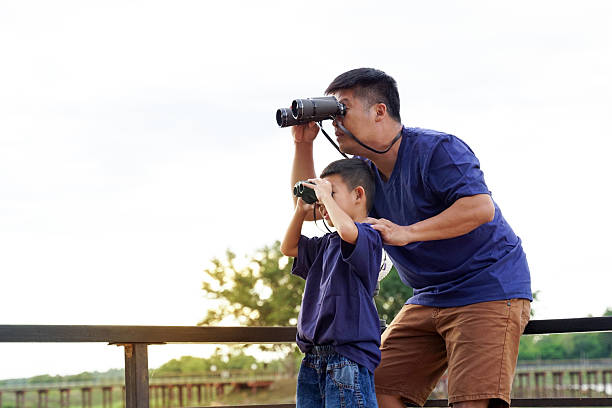 istock A father and his young son stand together, looking through binoculars, possibly birdwatching, against a bright outdoor sky. 2242413719