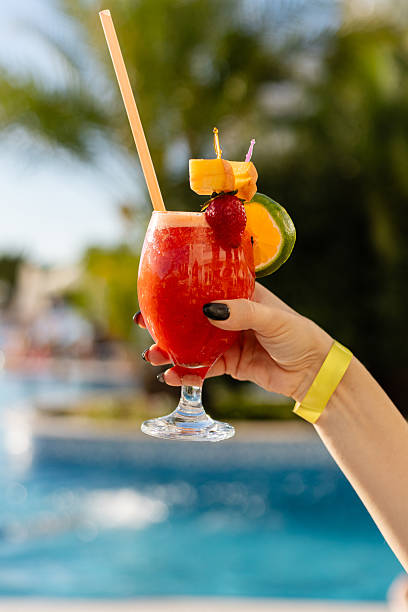 istock A hand holds a vibrant tropical drink adorned with fruit, enjoyed beside a sparkling blue pool under clear skies. The scene radiates summer vibes and relaxation. All inclusive concept. 2242414930