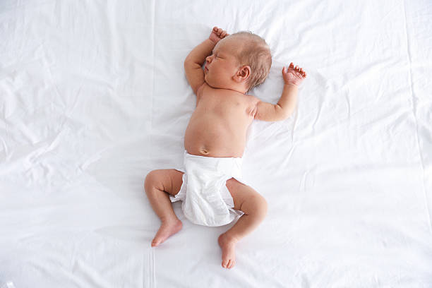 Adorable baby in white sunny bedroom. Newborn child relaxing in bed. Nursery for young children. Textile and bedding for kids. Family morning at home. New born kid during tummy time with toy bear.