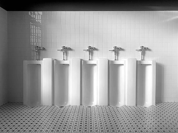 Guy taking a leak in public toilets. He is using standing toilet, looking down to see when he is done. Toilet is new, with sensors which detect when someone is going away from it.