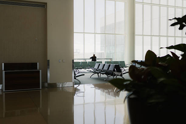 Person waiting in a minimalist and modern airport terminal, looking out of large windows with empty seating
