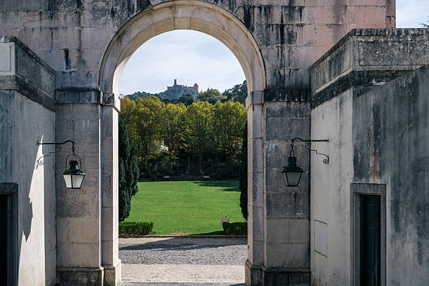 The colorful Pena Palace on a forested hill seen through a large stone archway in Sintra, Lisbon District, Portugal, on October 16, 2025.