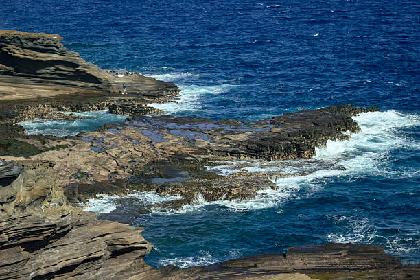 Ocean waves crash against dark volcanic cliffs of Hawaii, creating a dramatic contrast between the power of the water and the ancient stone formations along the island coast